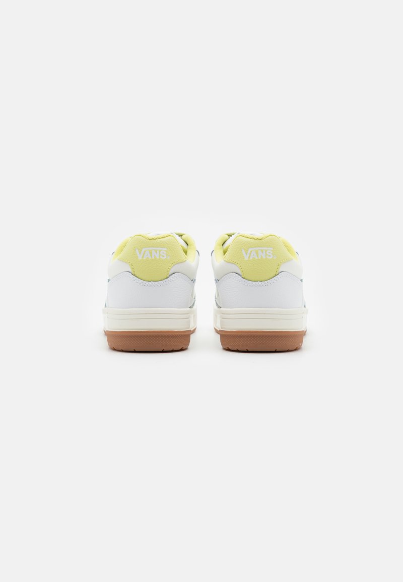 Zapatillas con parte superior de cuero blanco, detalles en amarillo claro y suela de goma. Cuenta con un collar acolchado y un logotipo prominente en la parte posterior.