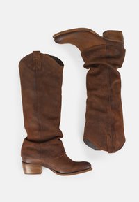 Bruine suède cowboylaarzen met een slouchdesign, puntige neus en gestapelde hak. Accenten omvatten contrasterende stiksels en trekbanden aan de bovenkant.