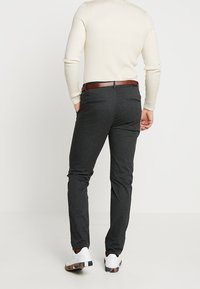 Mörkgrå byxor med smal passform, med bakfickor och ett brunt bälte, kombinerade med vita sneakers och en ribbad krämfärgad tröja.