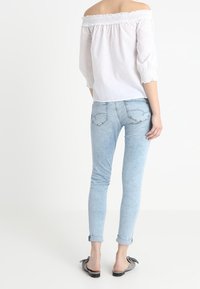 Blusa bianca scollata con elastico sul collo, maniche 3/4. Jeans aderenti azzurri con orli arrotolati, scarpe nere slip-on.