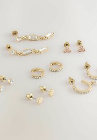 Set di orecchini in tono oro con disegni geometrici, pietre chiare e rosa, motivi floreali e vari stili di chiusura su uno sfondo chiaro.