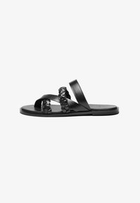 Black leather sandals featuring crisscross straps and a braided accent. Flat sole with a smooth texture, minimalistic design.