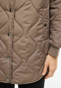 Ruda pankuota striukė su bangų raštu, su spaudėmis ir šoninėmis kišenėmis. Minkšta, blizgi medžiaga su briaunuotais rankogaliais ir laisvo silueto.