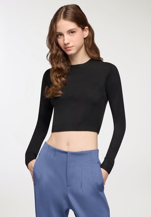 Maglione nero corto con maniche lunghe e scollo rotondo, abbinato a pantaloni su misura blu chiaro, dotati di tasche anteriori e una texture liscia.