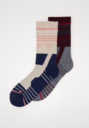Ein Paar Socken: ein beiges Paar mit navy, pink und weißen Mustern; das andere dunkelgrau mit burgunder und navy Streifen; gerippte Bündchen.