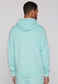 Sudadera verde menta con capucha ajustable, mangas largas, puños y dobladillo acanalados. Material suave de mezcla de algodón, textura lisa y corte relajado.