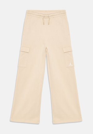 Pantalones cargo de pierna ancha en color beige con cintura elástica, cordón, bolsillos laterales con tapa y pequeño logo de Jumpman en blanco en el bolsillo derecho.