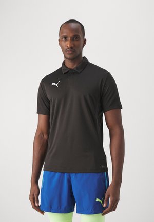 Sort polo shirt med tekstureret finish, udstyret med et hvidt Puma-logo på venstre bryst. Iført med blå shorts og neongrønne accenter.