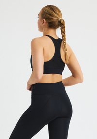 Sostén deportivo negro y leggings de cintura alta, ambos hechos de material elástico. Presenta un diseño de espalda nadadora y una textura suave.