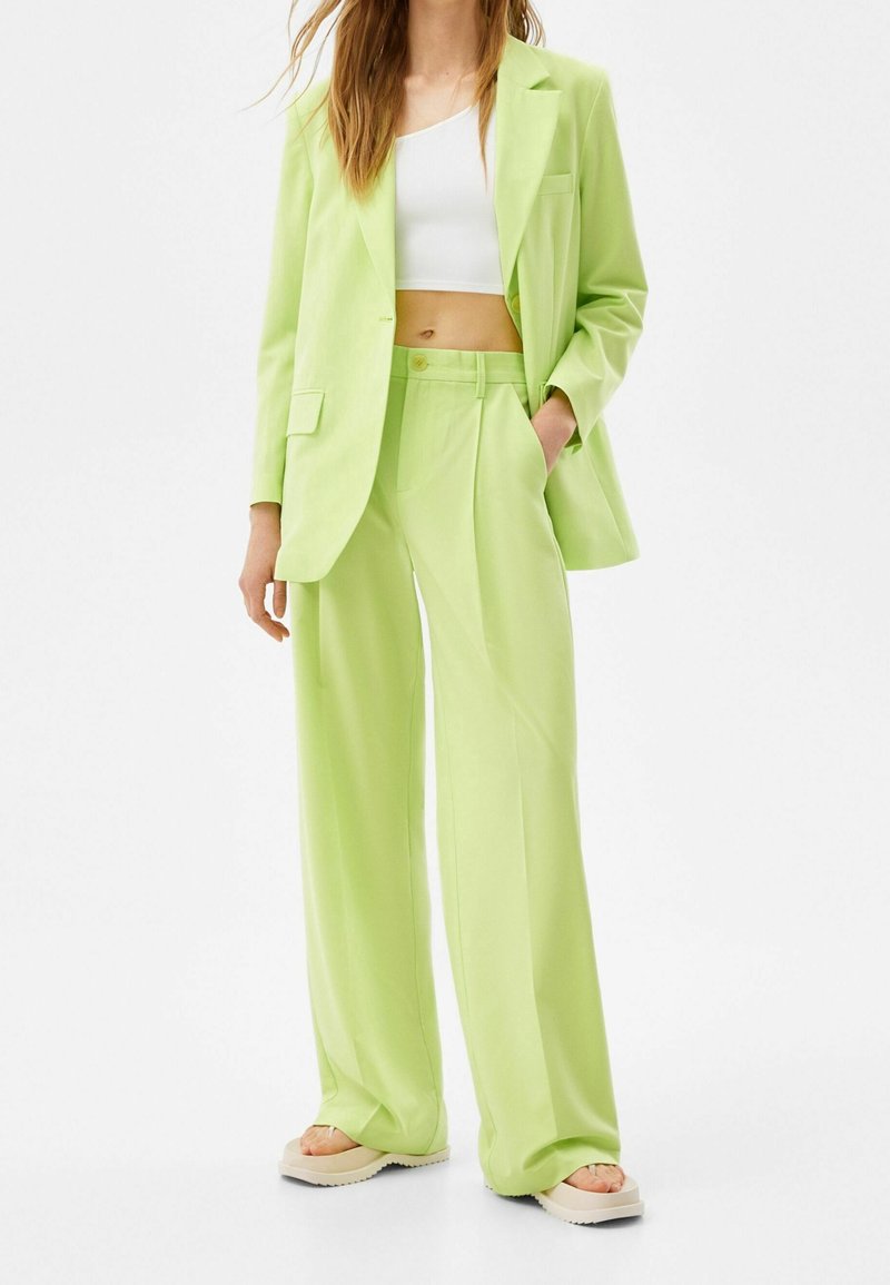 Blazer cintré vert clair avec un pantalon large assorti, associé à un crop top blanc. Tissu lisse avec une coupe décontractée et un design minimal.
