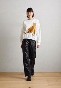 Felpa bianca con una grande illustrazione di un leopardo con macchie marroni, abbinata a pantaloni a gamba larga in ecopelle nera.