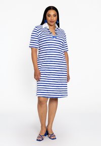 Gestreiftes Kleid aus blauem und weißem Baumwollstoff mit kurzen Ärmeln und Kragen. Kombiniert mit blauen Riemchen-Heels und auffälligen Ohrringen.