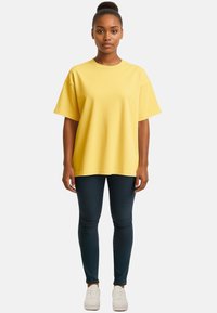 T-shirt oversize gialla con maniche corte e scollo rotondo; abbinata a jeans scuri e sneakers bianche. Tessuto morbido, vestibilità casual.