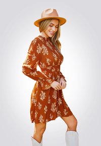 Vestido en tono óxido con estampado floral, de mangas largas y cintura fruncida. Combinado con un sombrero beige y botas altas blancas.