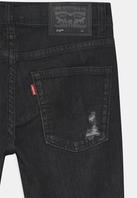 Black denim jeans with a slim fit, featuring a distressed detail on the back pocket and a black label on the waistband.