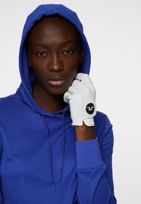 Blå huvtröja med snörning och strukturerad vit handske med en svart cirkulär logo. Materialen verkar mjuka och släta.