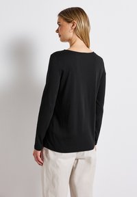 Schwarzes Langarmshirt mit Rundhalsausschnitt, glatter Textur und lockerer Passform. Besitzt ein schlichtes Design und minimale Steppnähte am Saum.