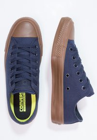 Baskets en toile navy avec un embout et une semelle en caoutchouc marron. Équipées de lacets ronds, d'œillets et d'une doublure intérieure jaune vif avec le logo de la marque.