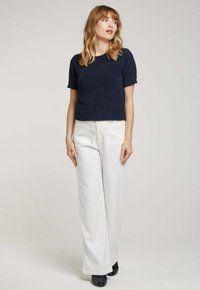 Pull en maille texturée bleu marine à manches courtes associé à un pantalon blanc à jambes larges et des bottines noires. Design simple sans motifs visibles.