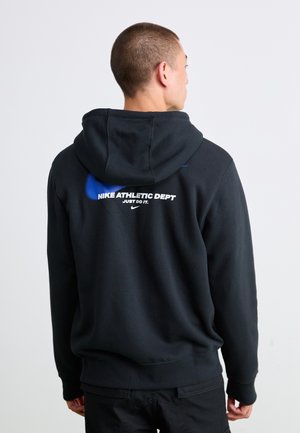 Man wearing black hoodie with blue Nike logo and white "Nike Athletic Dept Just Do It" text, facing away against plain background.