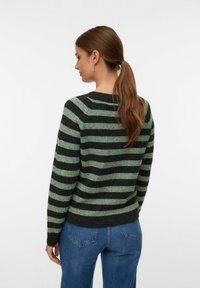 Pullover a righe in verde scuro e nero, con scollatura arrotondata e maniche lunghe. Il tessuto appare morbido e strutturato, abbinato a jeans blu.