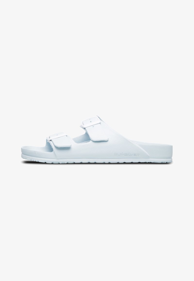 White slip-on sandals made of soft plastic, featuring two adjustable straps and a textured sole for grip. Minimalist design with no embellishments.