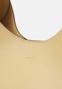 Geel lederen tas met een gladde textuur, voorzien van een gebogen vorm en een geperst 'Coach New York' logo. Subtiele stiksels zijn zichtbaar.