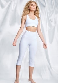 Biały sportowy biustonosz i legginsy o wysokim stanie w formie capri, oba wykonane z gładkiego, elastycznego materiału. Projekt jest bezszwowy z dopasowanym krojem.