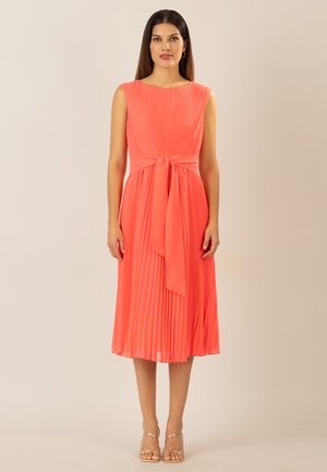 Korallenfarbenes plissiertes Kleid mit tailliertem Oberteil, rundem Ausschnitt und Taillengürtel. Glatter Stoff, knielanger Saum und minimales Zubehör.