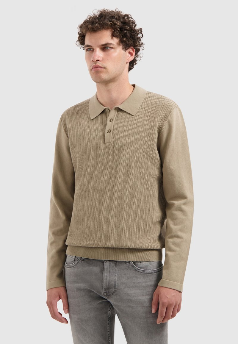 Beige Langarm-Polohemd mit strukturiertem Strickdesign, Drei-Knopf-Leiste sowie geripptem Kragen und Bündchen, kombiniert mit grauen Jeans.