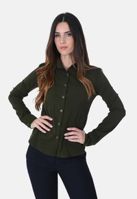 Camicia button-up verde scuro con maniche lunghe, slim fit e texture liscia. Presenta un colletto e bottoni lungo la parte frontale.
