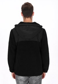 Chaqueta de forro polar negra con capucha, con canesú de tela negra lisa, cuerpo texturizado y mangas largas; diseñada para brindar calor y comodidad.