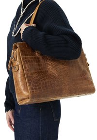Bruine leren handtas met een krokodillenstructuur, voorzien van een bovenhandgreep en een ritssluiting, gedragen op de schouder van een persoon.