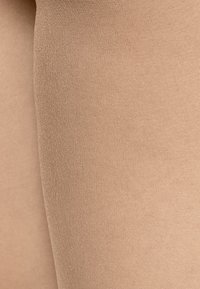 Collant color nude con una texture liscia e opaca, caratterizzati da un design senza cuciture e da una leggera lucentezza, progettati per il comfort e la vestibilità.