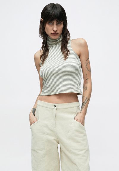 Ριγωτό ριμπ ζιβάγκο χωρίς μανίκια σε ανοιχτό πράσινο και λευκό, συνδυασμένο με κρεμ παντελόνι από κοτλέ με φαρδιά μπατζάκια και μεγάλα τσέπες.