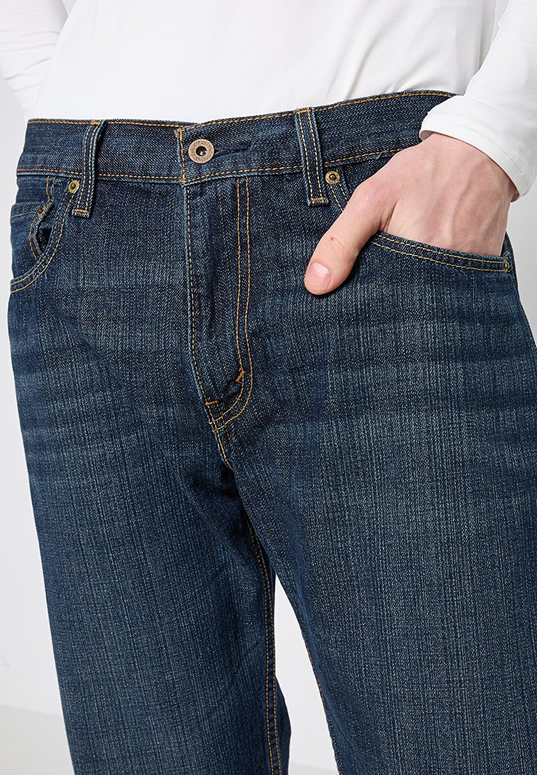 Jean en denim bleu foncé avec une coupe droite, doté de coutures jaunes, d'une fermeture à bouton en métal et de poches avant.