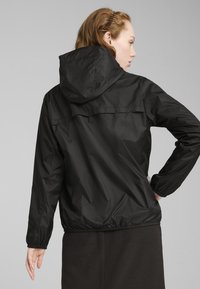 Veste noire légère avec capuche. Élastiques aux poignets et à la taille. Texture lisse, design minimaliste avec un détail de empiècement dans le dos.