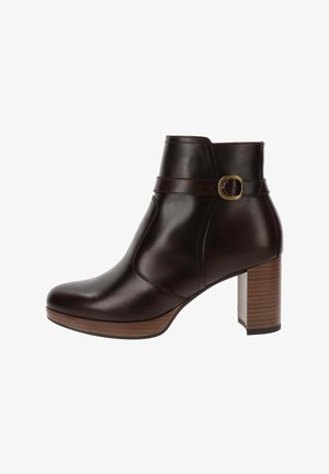 Bottine en cuir marron avec un bout rond, un large talon bloc, et une sangle décorative avec une boucle en métal autour de la cheville.
