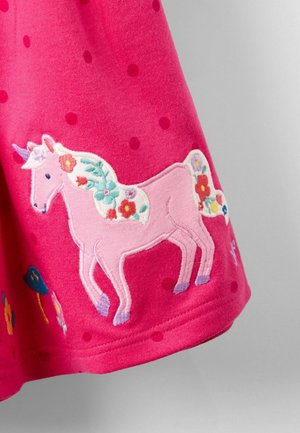 Helles pinkes Stoff mit Punkten, das ein gesticktes pinkes Einhorn mit floralem Mähne und bunten Akzenten an einem geschwungenen Saum zeigt.