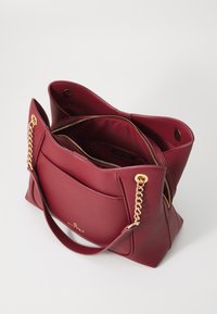 Sac fourre-tout en faux cuir rouge texturé avec des accents en chaîne dorée, des compartiments zippés et une poche centrale. Ouverture en haut avec un intérieur spacieux.