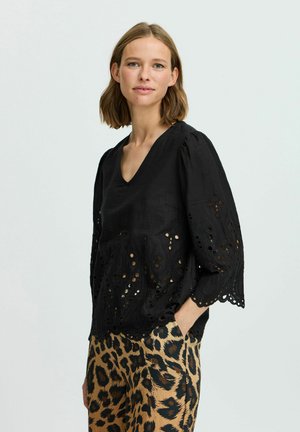 Blouse noire avec un décolleté en V, manches bouffantes trois-quarts et des détails en découpe laser le long de l'ourlet. Associée à un pantalon à imprimé léopard.