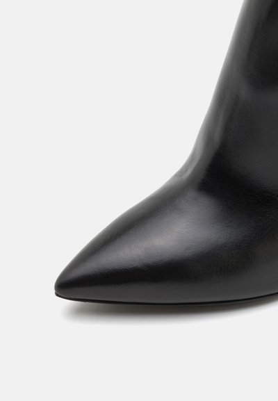 Pantof cu toc înalt din piele neagră, cu vârf ascuțit. Suprafață elegantă, cu textură netedă și design minimalist.