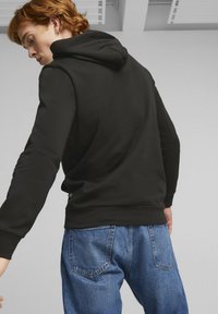 Felpa nera con una texture morbida, dotata di cappuccio e maniche lunghe, abbinata a jeans in denim blu con tasche posteriori e dettagli di cucitura.