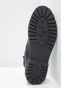 Černá gumová podešev s texturovaným vzorem a vyvýšenými hexagonálními akcenty. Boční strana je vyrobena z kombinace semiše a síťoviny.