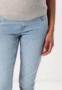 Jeans de mezclilla azul claro con un diseño ajustado, que cuentan con bolsillos y una textura suave. Llevados con una camiseta gris, con detalles mínimos visibles.