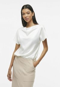 Hvit satengbluse med korte ermer og drapert halslinje, kombinert med en beige, tettsittende blyantskjørt med frontlommer og glatt tekstur.