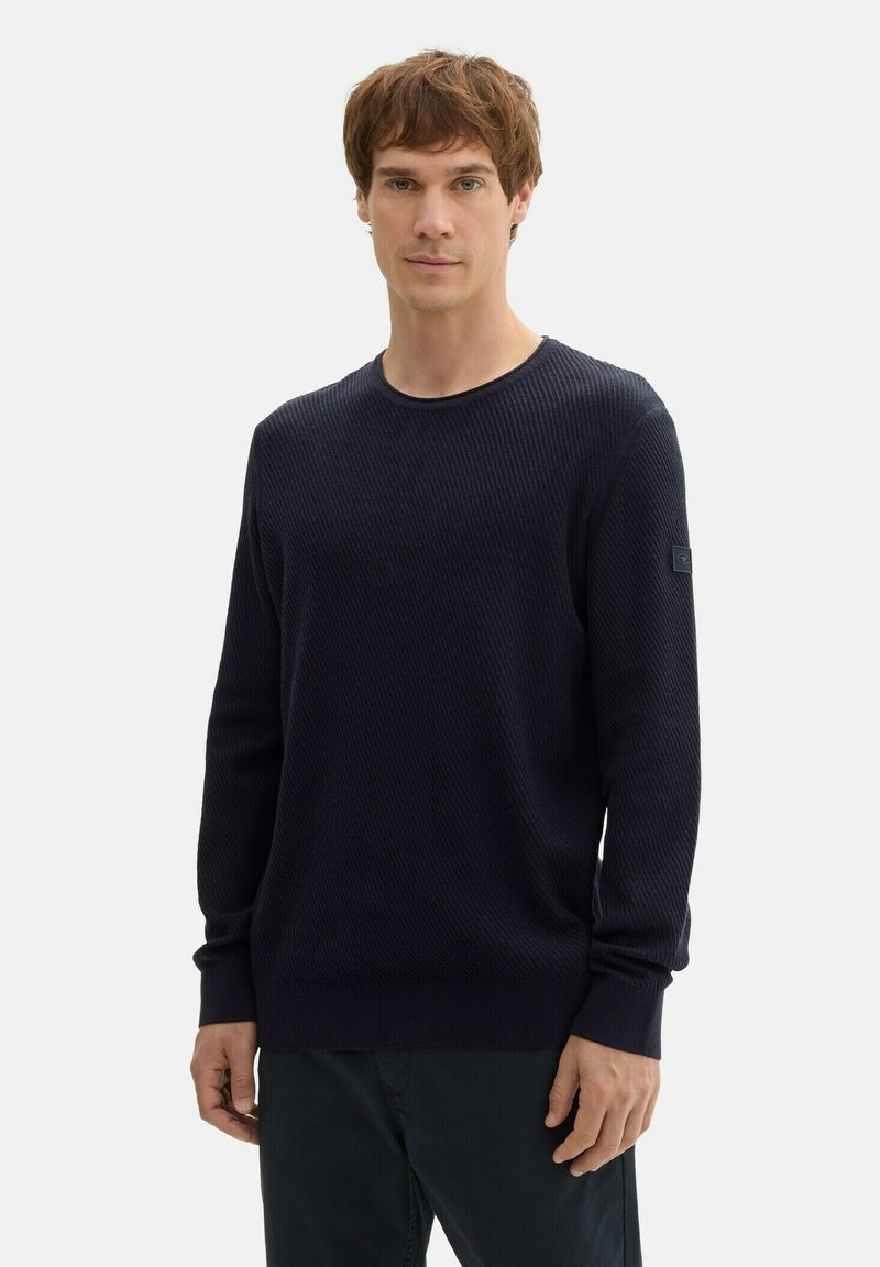 Dunkelblauer Rundhals-Pullover mit strukturiertem Rippstrickdesign, langen Ärmeln und schmaler Passform. Mit einem schwarzen Logo-Patch am linken Arm.