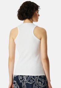 White sleeveless tank top with a fitted design, smooth cotton texture, and high neckline, paired with patterned dark blue pants with stars.