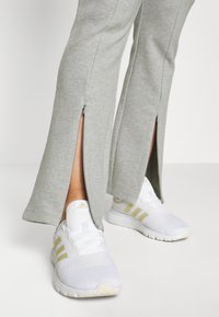 Grijze sweatpants met zijritsen, gecombineerd met witte sneakers met gouden accenten en merklogo. Focus op sportief, casual ontwerp en stoftextuur.