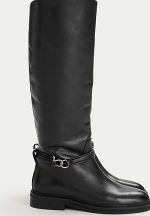 Black knee-high leather boots with flat soles and decorative silver bit detail around the ankle.